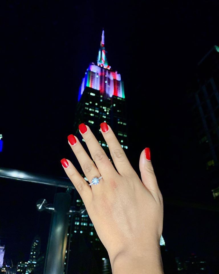 A lady holding up her new engagement ring in front of the Empire State Building in New York City